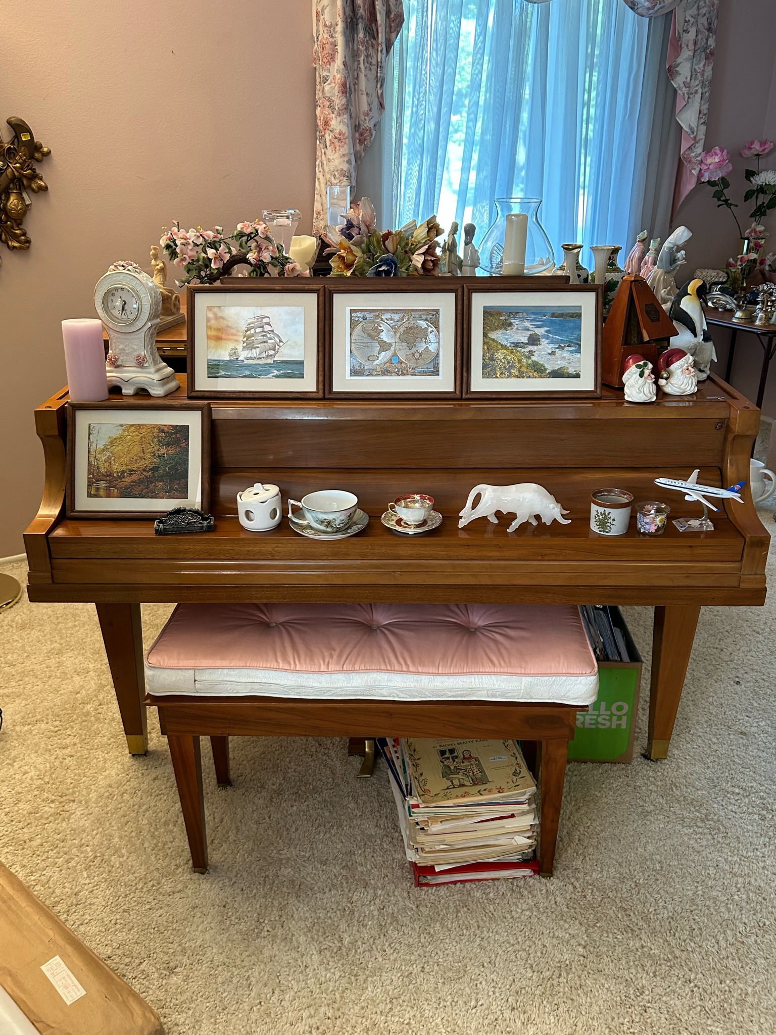 A wooden baby grand piano is displayed with numerous paintings and decor pieces.